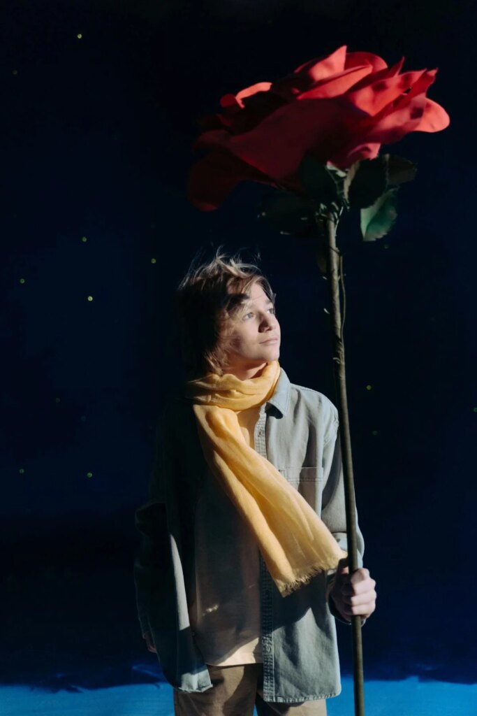 Boy with yellow scarf holding a red flower