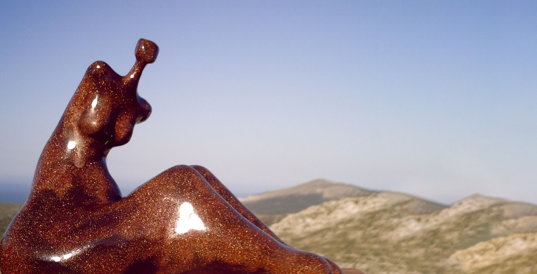 Escultura de mujer sentada horizontal frente a montaña para contacto
